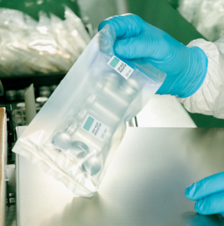 Eine Person mit blauen Handschuhen hält im Sauberraum ein steril verpacktes Set von Glasvials. | © © infochroma ag